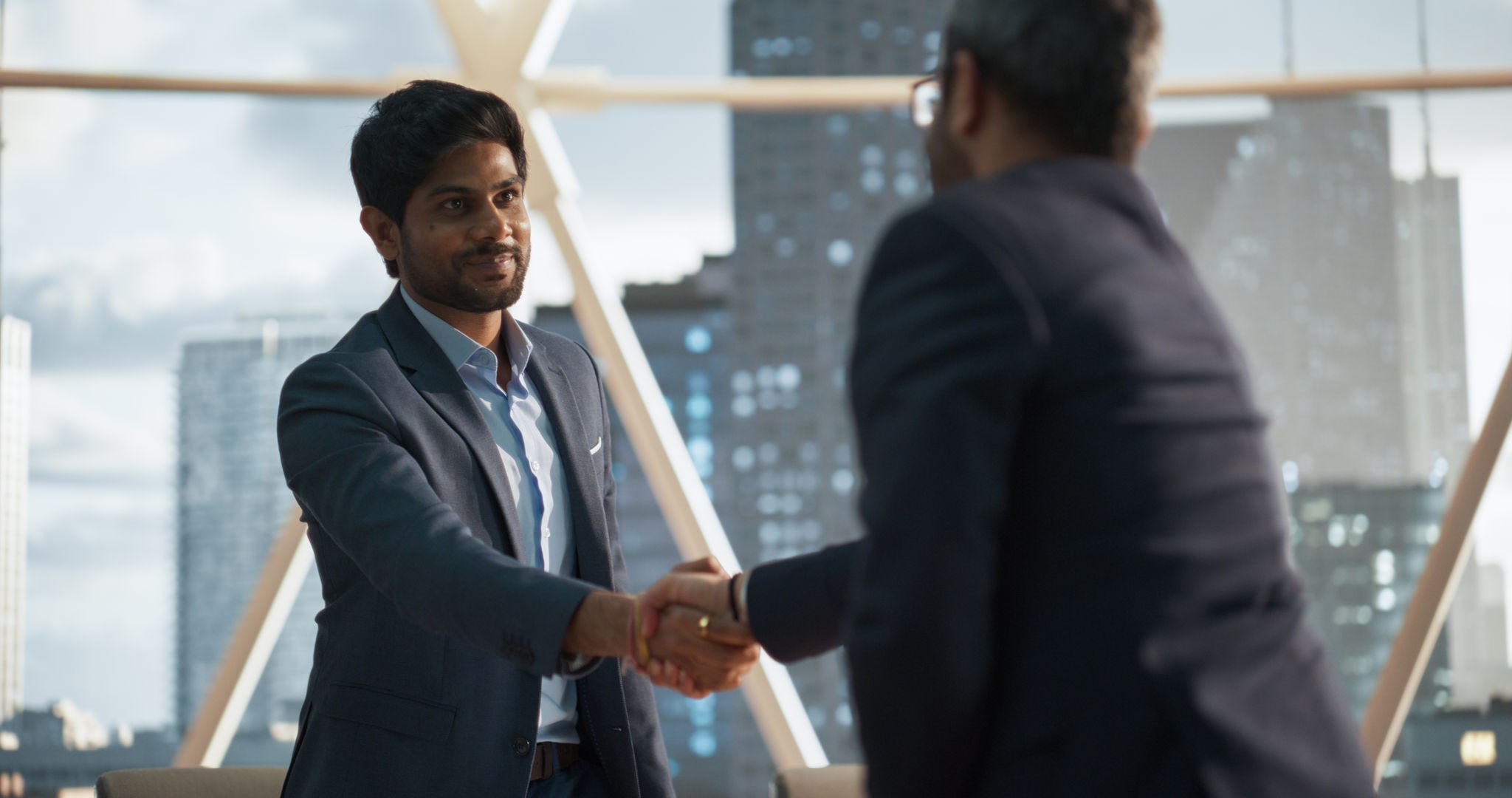 Young Indian Businesspeople Closing a Business Deal at a Meeting Room in Corporate Modern Office. Two Men in Classic Suits Shake Hands and Celebrate Successful Partnership