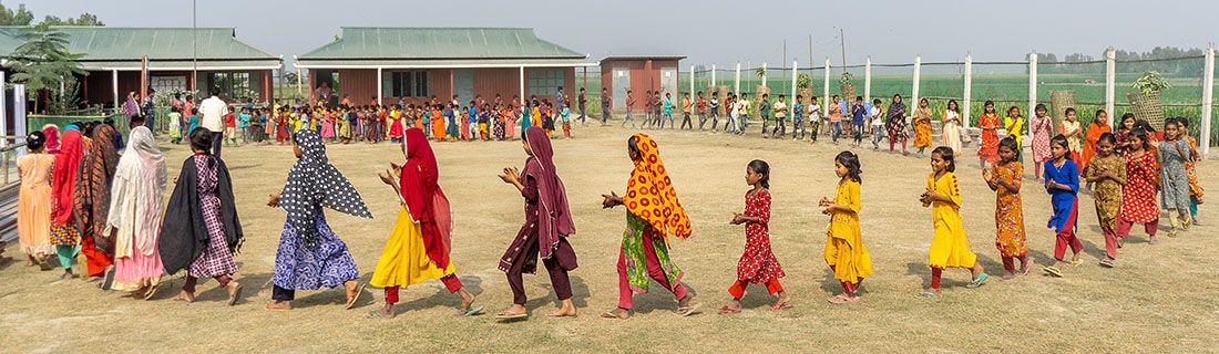 Group of kids on a field walking together in a circle clapping their hands.