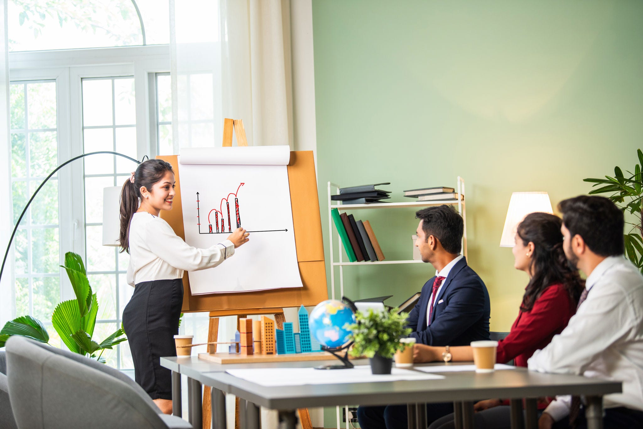 Confident Indian asian male or female boss or trainer make whiteboard presentation at team office meeting