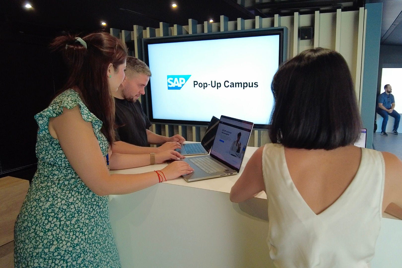 Drei Leute schauen auf einen Bildschirm mit SAP Logo