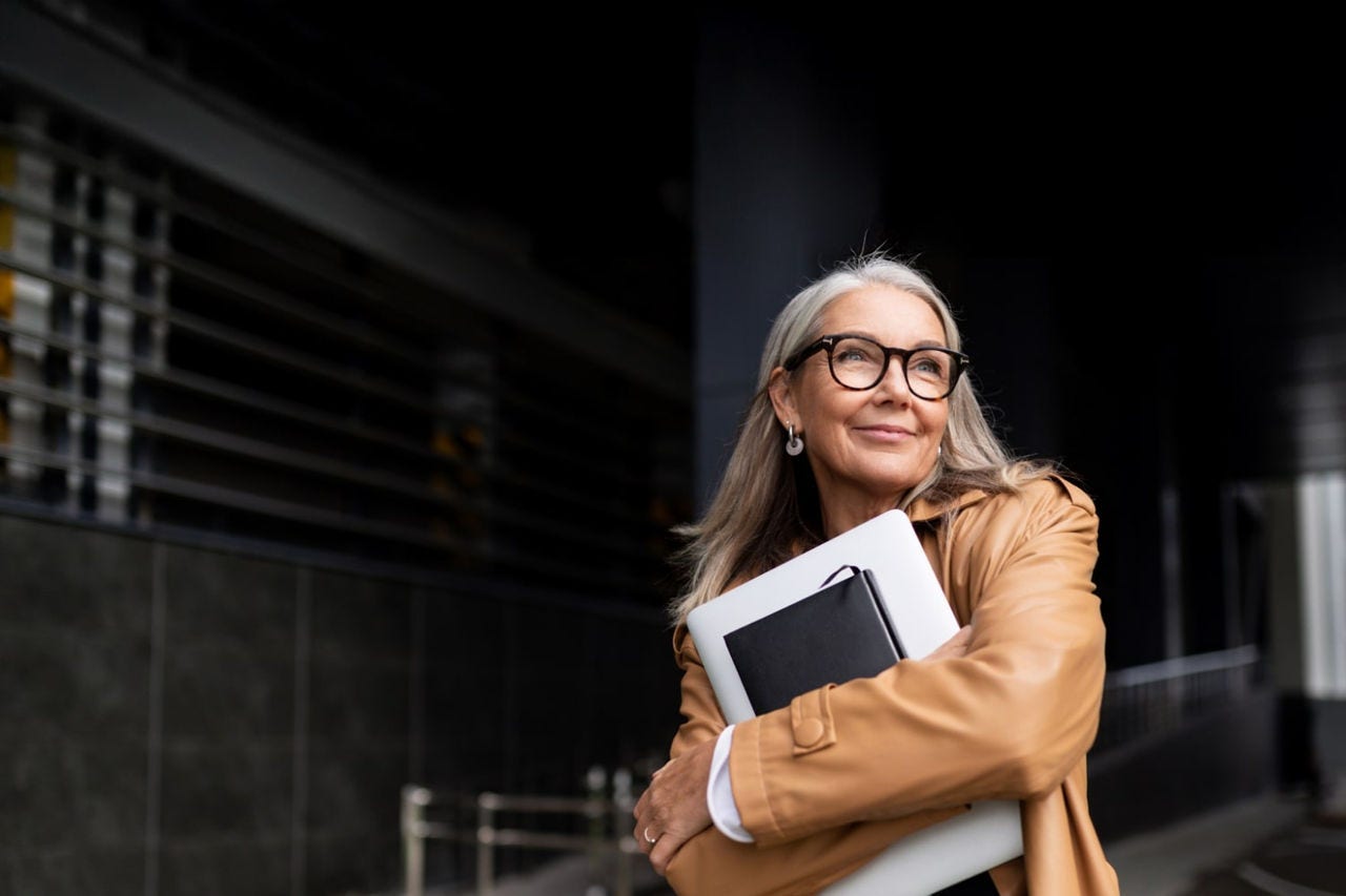 Woman wearing glasses holding laptop and diary in her arms