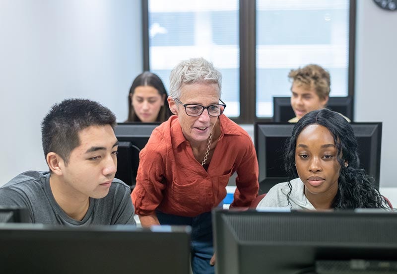 IAP social infrastructure image High school teacher helping students with assignment in computer lab