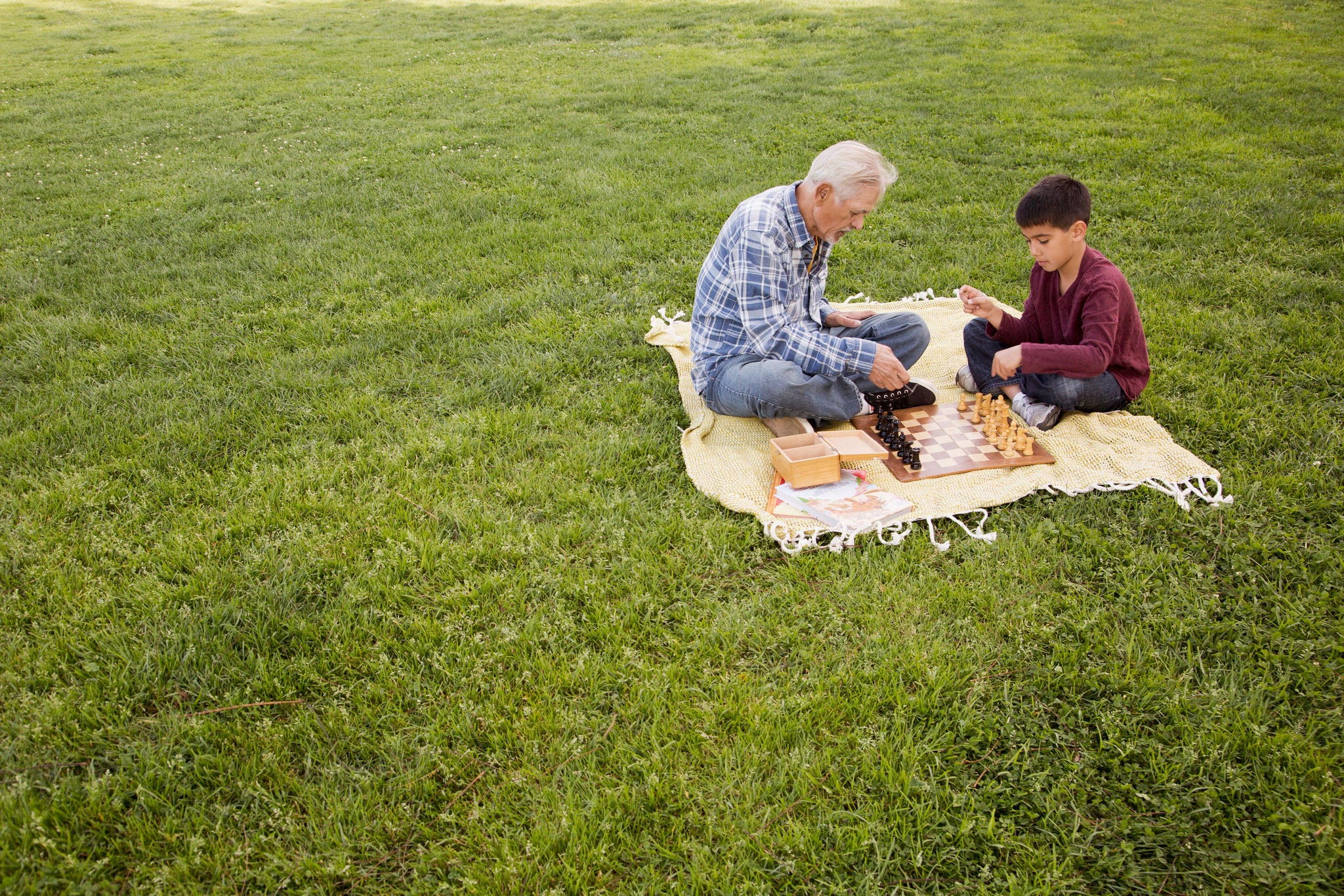 Older Hispanic man and grandson playing chess in park. Keywords: Chess, Child, Grandfather, Senior Adult, Elevated View, Grass, Childhood, Competition, Latin American and Hispanic, Full Length, Outdoors, 70-79 Years, Copy Space, Adult, Bonding, Grandson, Multi-Generation Family, Sitting, Togetherness, Chess Piece, Cross-legged, Males, Retirement, Leisure Games, Men, 6-7 Years, Active Seniors, Affectionate, Blanket, Boys, Brown Hair, California, City Of Los Angeles, Colour Image, Day, Enjoyment, Horizontal, Leisure Activity, Lifestyles, Looking Down, Love, Nature, People, Photography, Primary Age Child, Senior Men, The Ageing Process, Two People, USA, Weekend Activities 