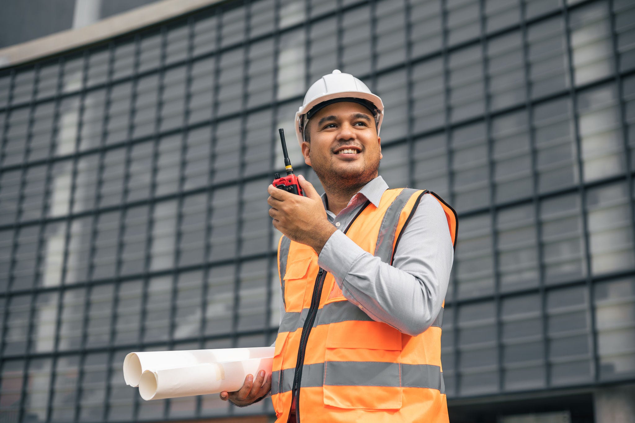 Asian engineer holding radio operate and control the worker employee to build construction. Young  indian architecture working at modern building construction site talking with radio.