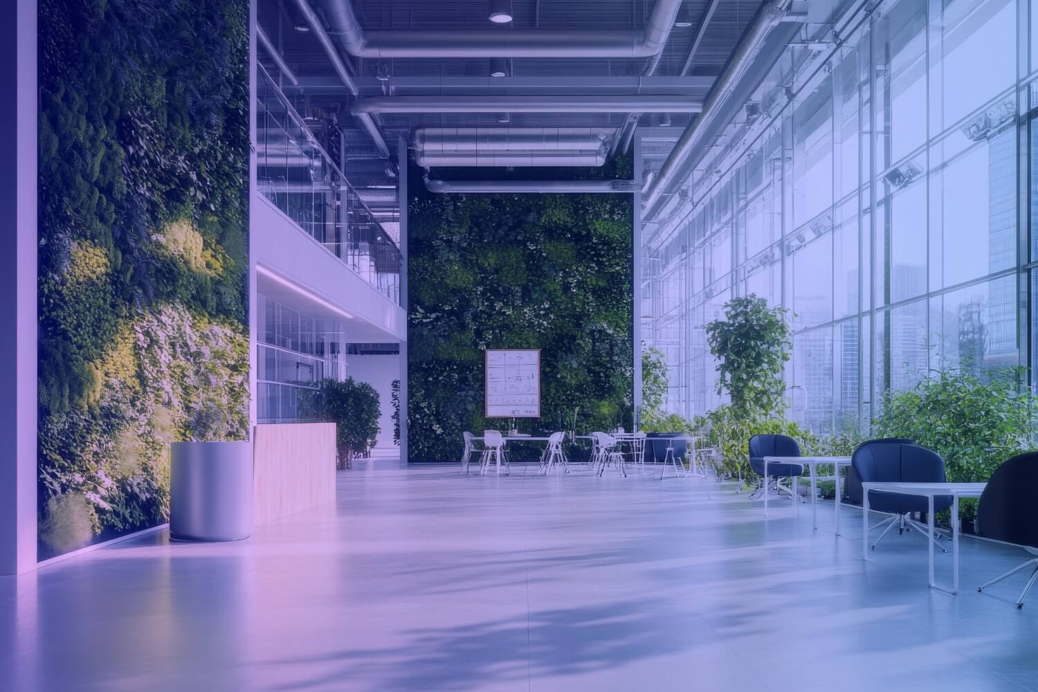 A modern, bright atrium with large windows, seating areas and several green walls covered with plants.