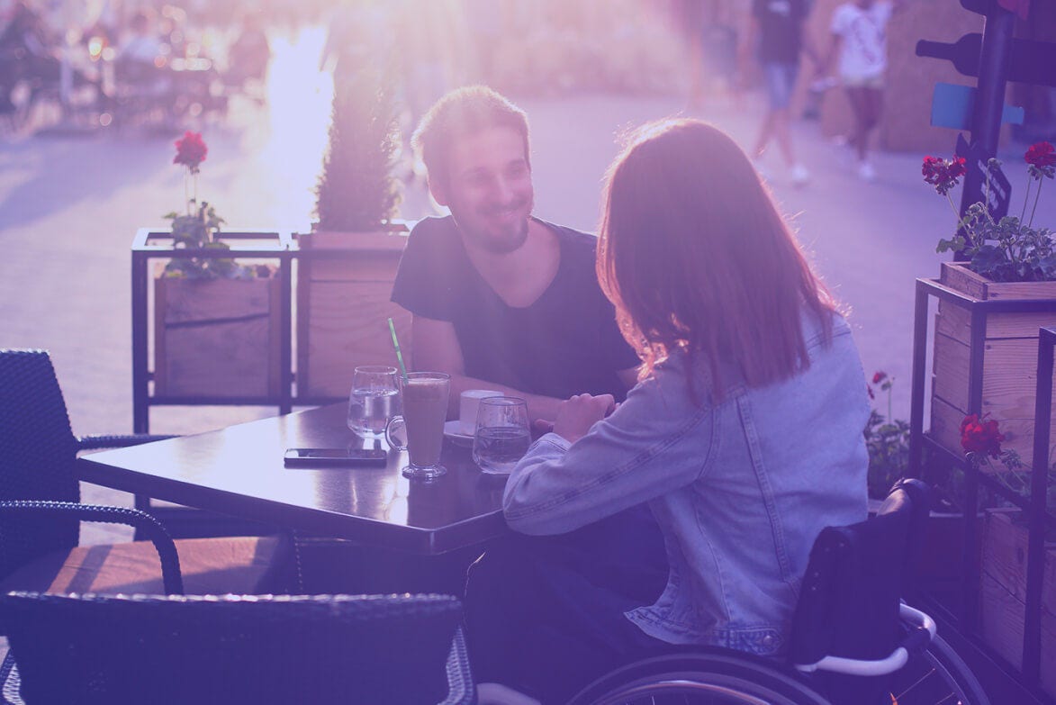 Woman in a wheelchair and man chatting at an outdoor café.