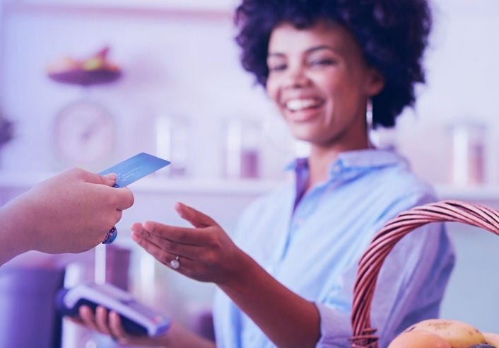 Shot of a female juice bar owner taking payment from customer. Female customer paying for juice with credit card.