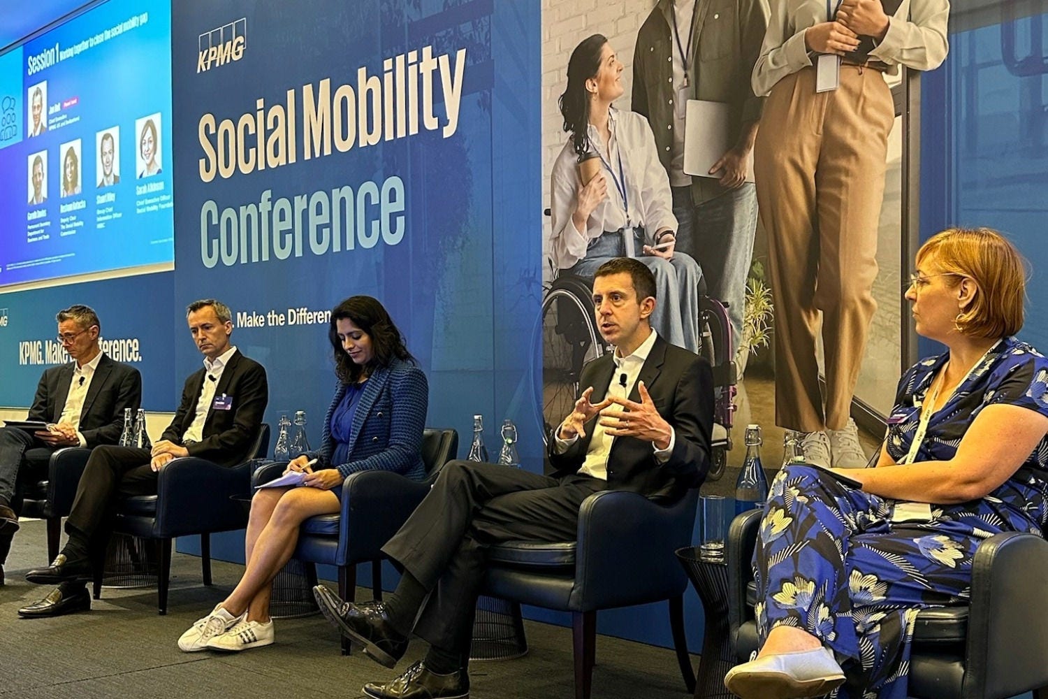 A group of people sat on a stage in front of a KPMG Social Mobility Conference sign