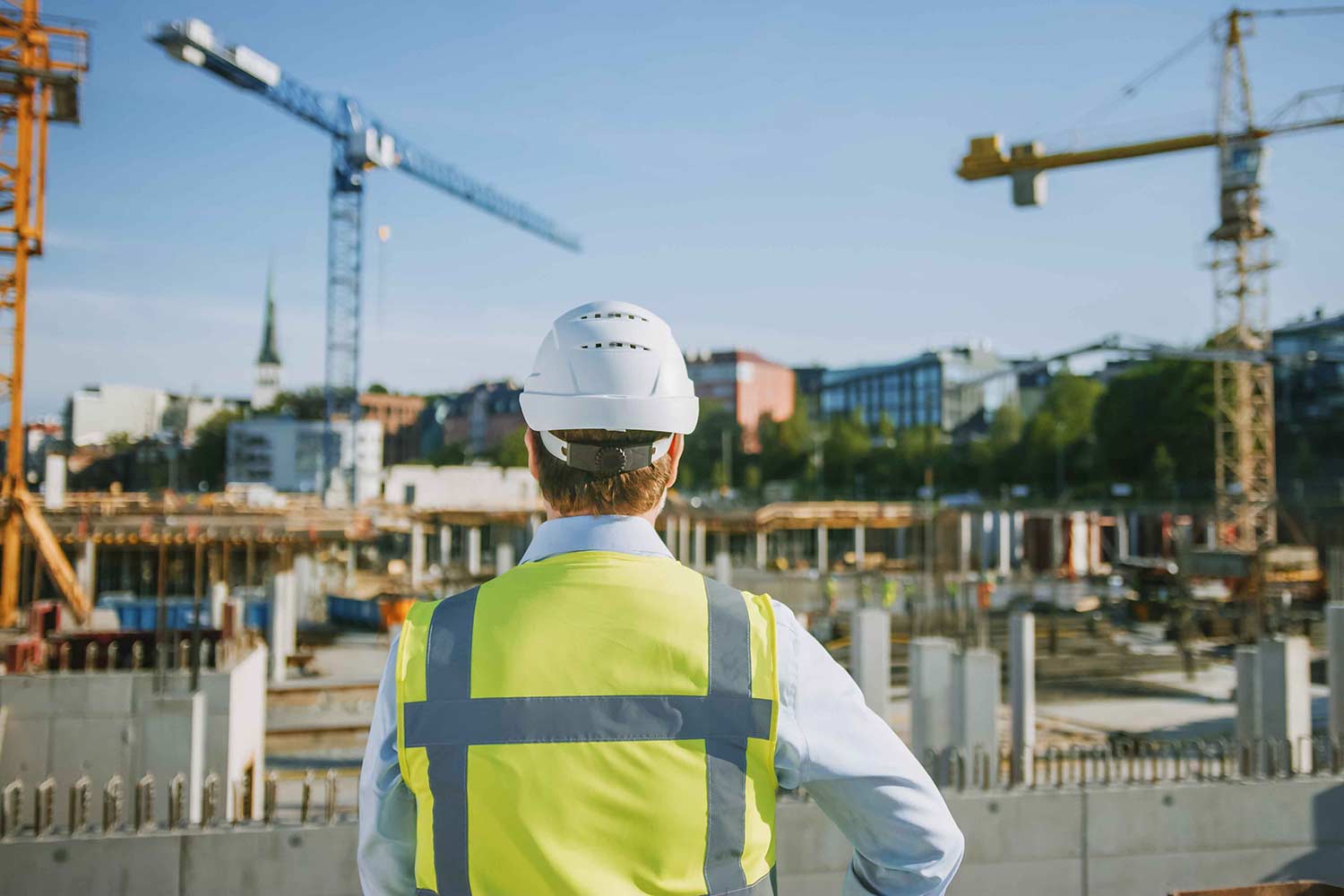Man in hard hat and vis vest overlooking building site representing cost management
