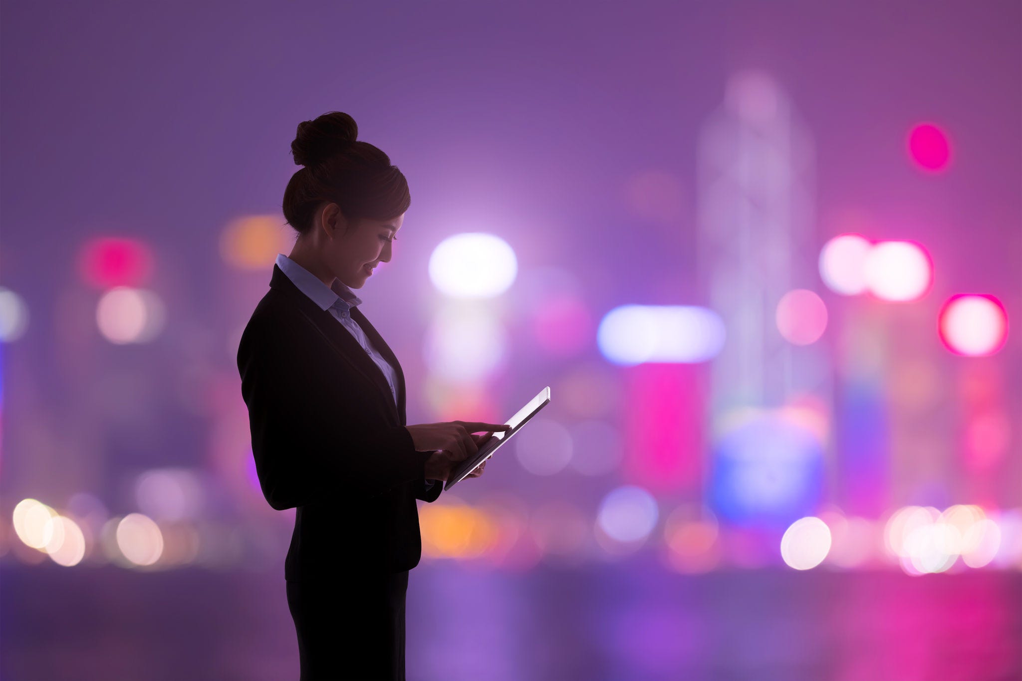 Woman using a tablet with the silhouette of a city at night in the background