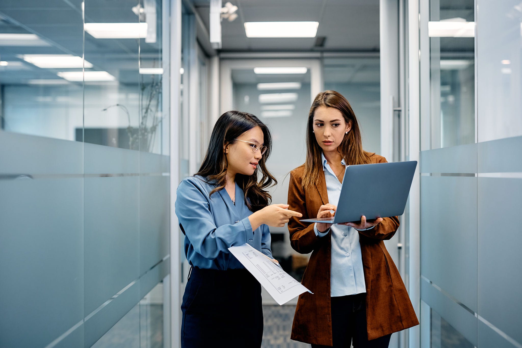 Young businesswomen cooperating while working on laptop in hallway.