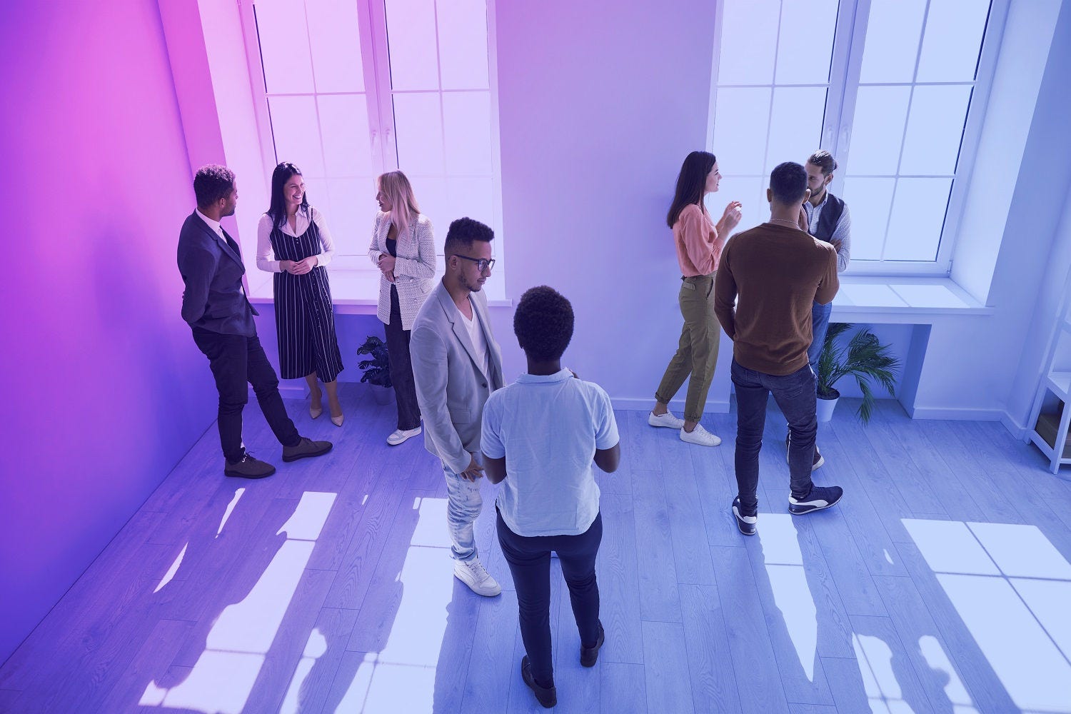 A diverse group of people conversing in a room lit by natural light.