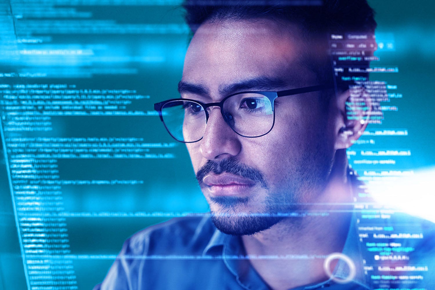 Man with glasses looking at code reflected on a computer screen