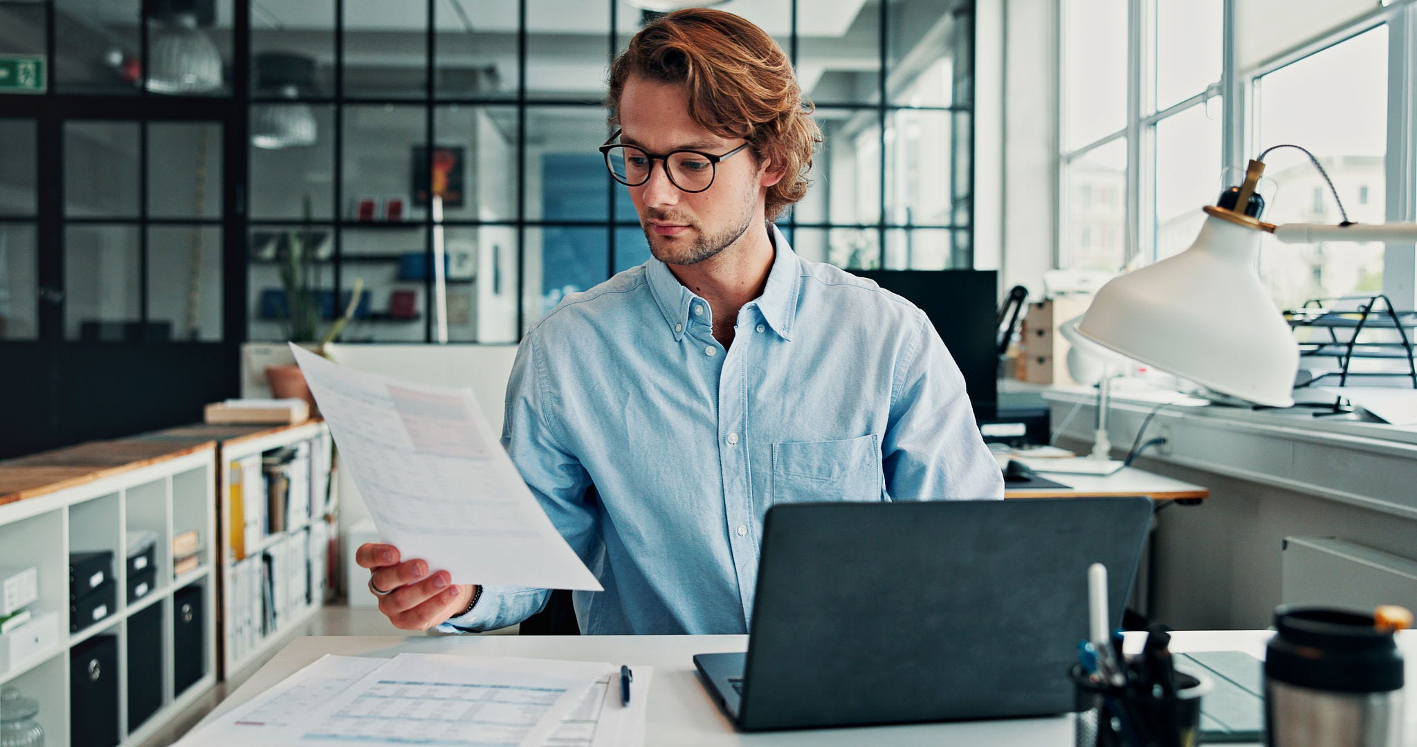 Review, document and man in office with laptop, glasses or preparation of financial statement. Reading, audit paper or analyst in workplace with tech, data entry or balance sheet in budget management