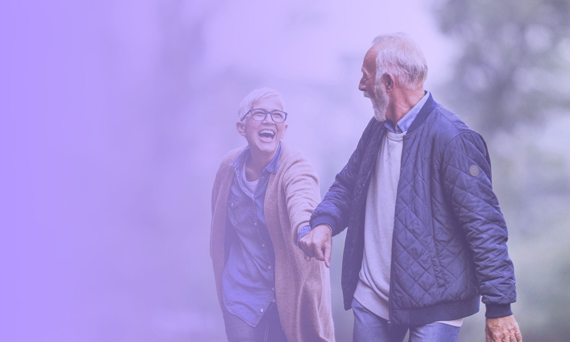 An older couple laughing while walking through a park An older couple laughing while walking through a park