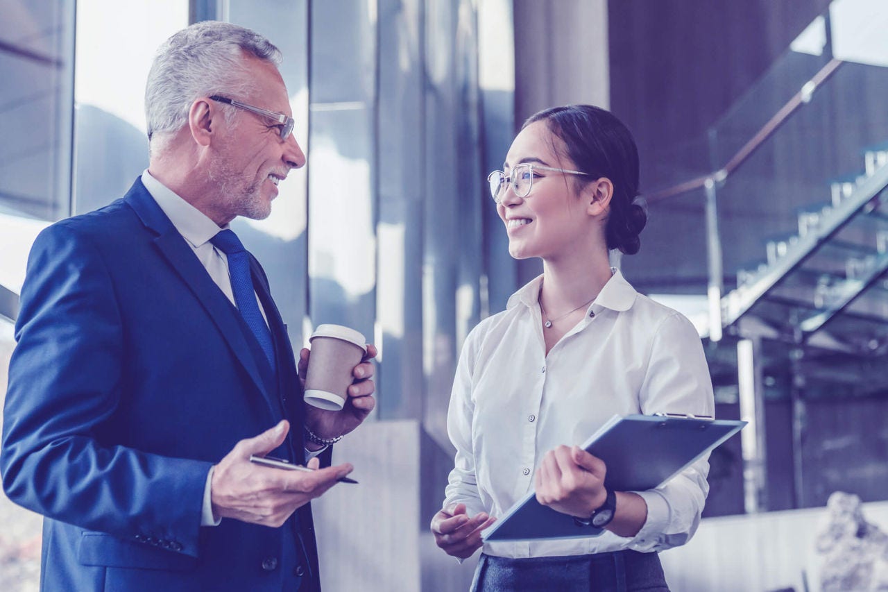 Two colleagues talking and smiling in the lobby of a business building.