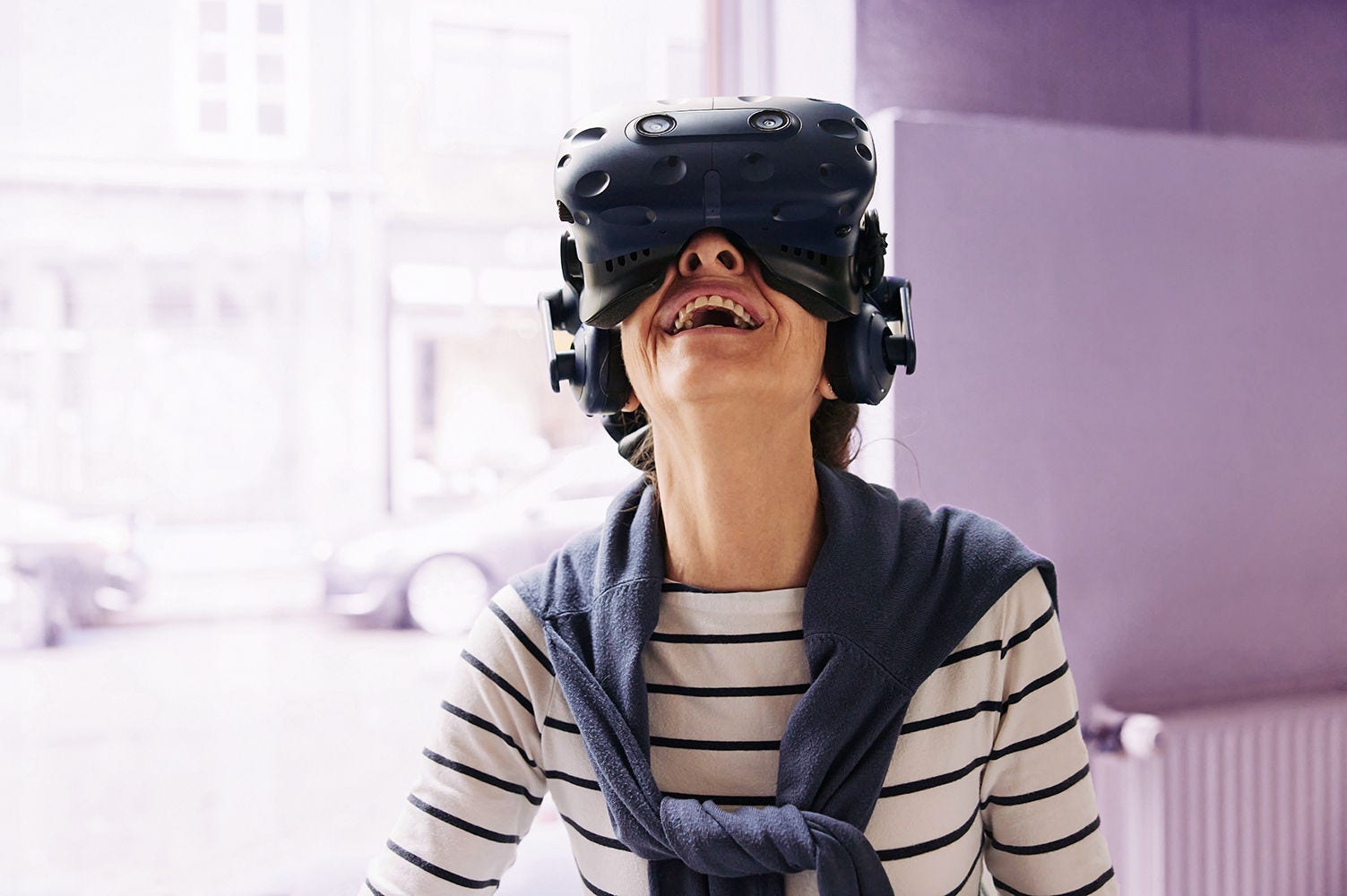 Senior woman laughing while having fun exploring a virtual world using a vr headset at a vr club; Shutterstock ID 2238971735; purchase_order: advisory assurance; job: anne; client: ai