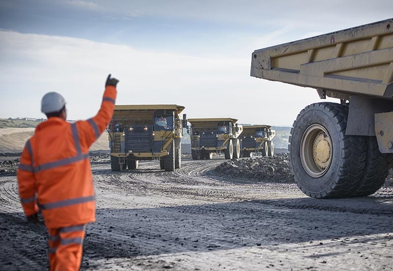 IAP mining image Mine worker waving at dumpers driving on track at surface coal mine