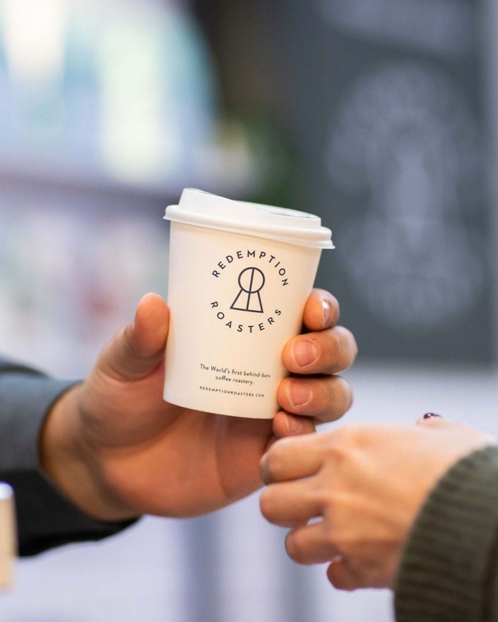 Redemption Roasters coffee cup being handed from one person to another