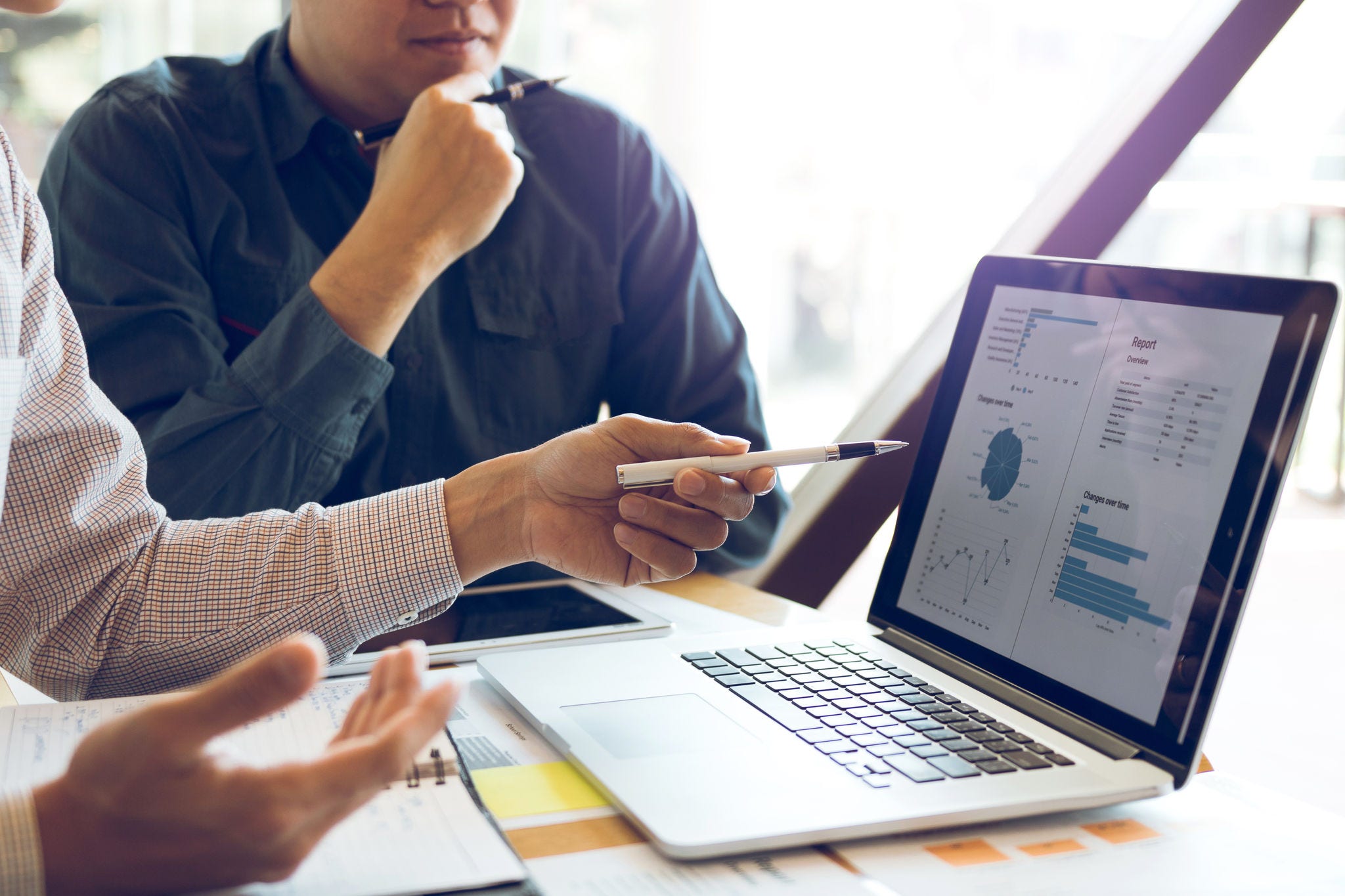 Two businessmen are together analyzing the financial data graph and pointing to the laptop computer screen.