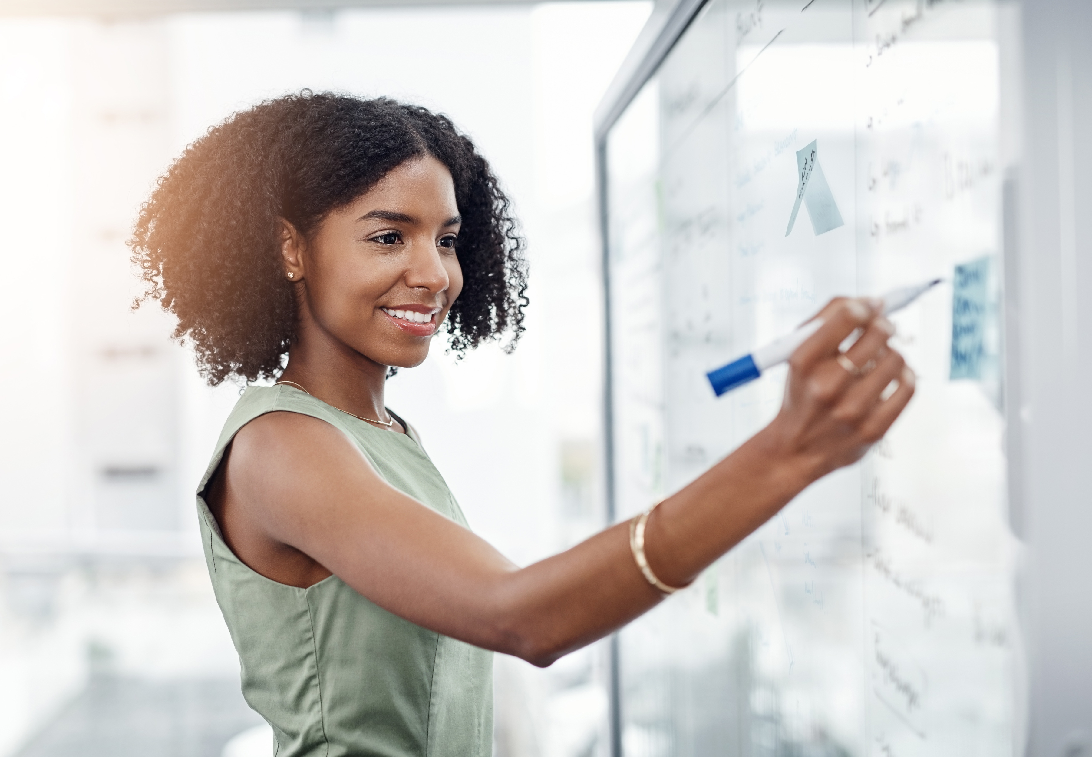 Business, glass wall and black woman writing, plan or strategy in office. Brainstorming, board and happy female person write idea, working on project and schedule, notes or information in workplace